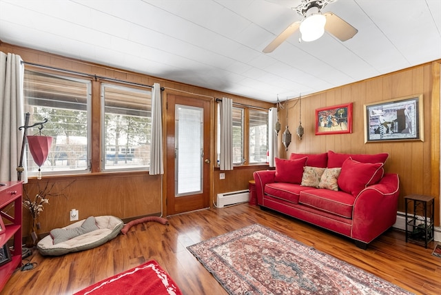 living area with ceiling fan, wooden walls, baseboard heating, and wood finished floors