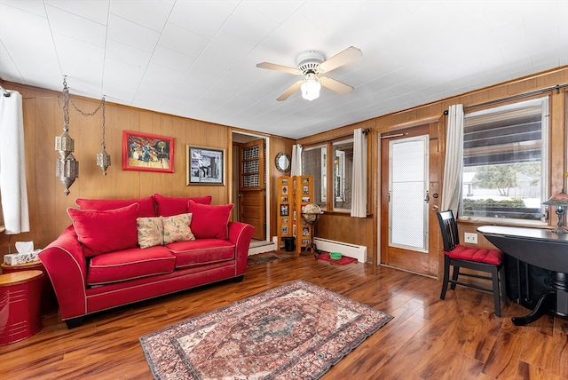 living room featuring a baseboard radiator, a baseboard heating unit, ceiling fan, wooden walls, and wood finished floors