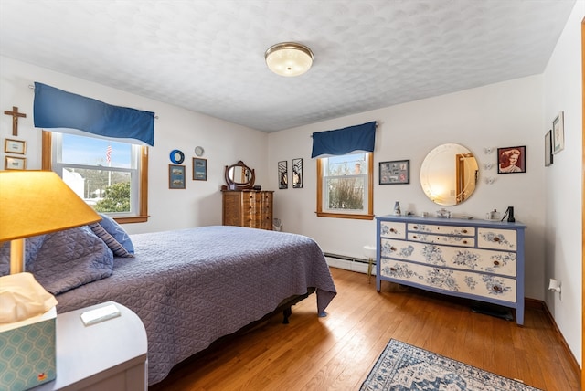 bedroom with a baseboard radiator, multiple windows, a textured ceiling, and hardwood / wood-style flooring