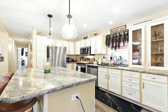 kitchen with a center island, light stone countertops, a breakfast bar area, appliances with stainless steel finishes, and a sink