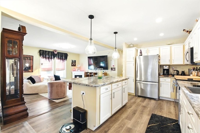 kitchen featuring stainless steel appliances, open floor plan, white cabinets, and light wood-style flooring