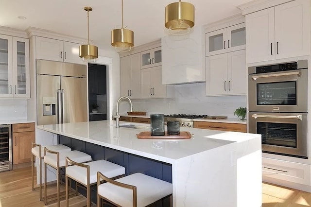 kitchen featuring appliances with stainless steel finishes, light hardwood / wood-style floors, sink, an island with sink, and decorative backsplash