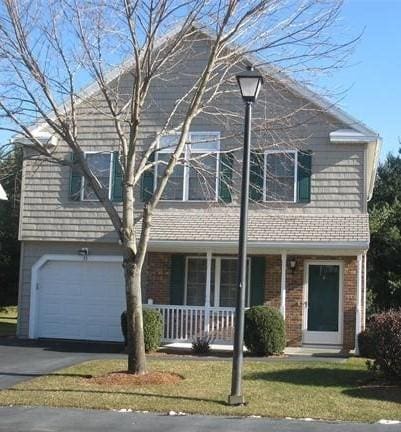 view of front facade with a porch, an attached garage, brick siding, driveway, and a front lawn