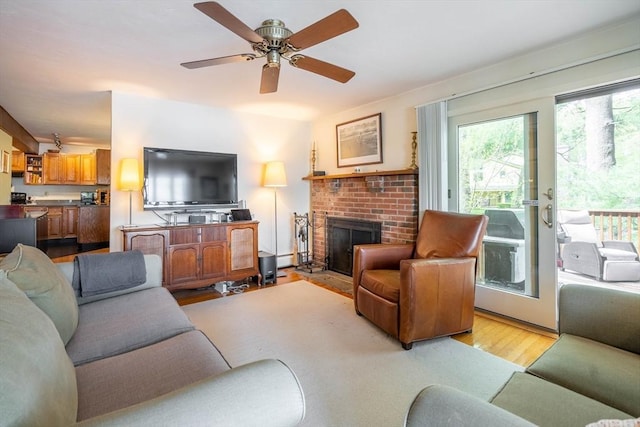 living room featuring light wood-style floors, a brick fireplace, and a ceiling fan