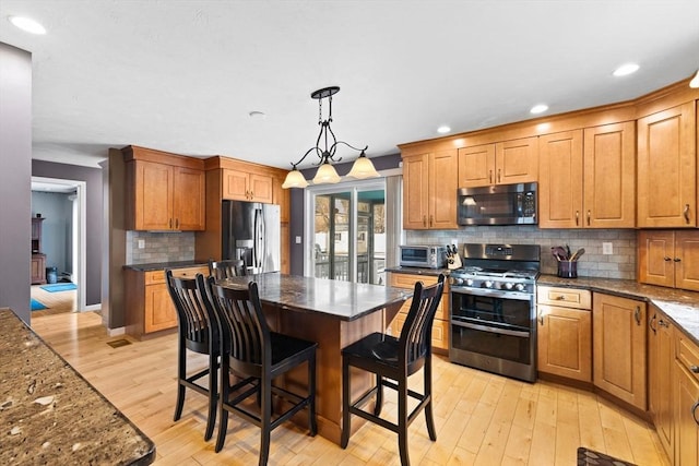 kitchen with decorative light fixtures, a center island, light hardwood / wood-style flooring, a kitchen breakfast bar, and stainless steel appliances