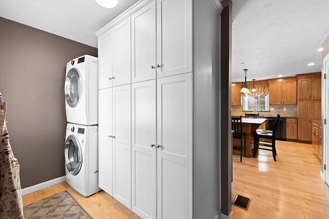 laundry area featuring cabinets, stacked washer and clothes dryer, and light wood-type flooring