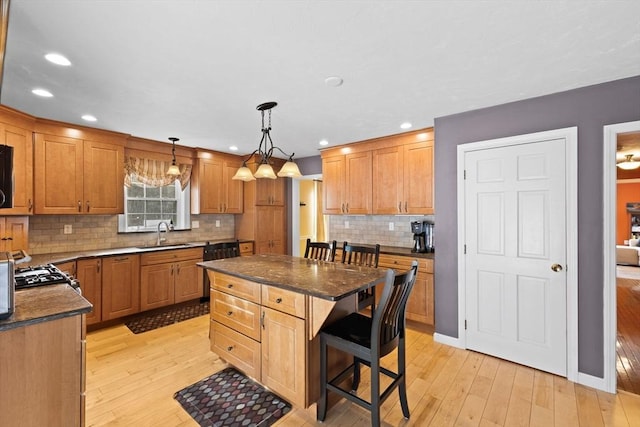 kitchen featuring decorative light fixtures, sink, a kitchen bar, a center island, and light wood-type flooring