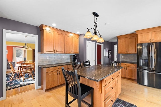 kitchen featuring a breakfast bar, hanging light fixtures, a center island, black fridge with ice dispenser, and light wood-type flooring