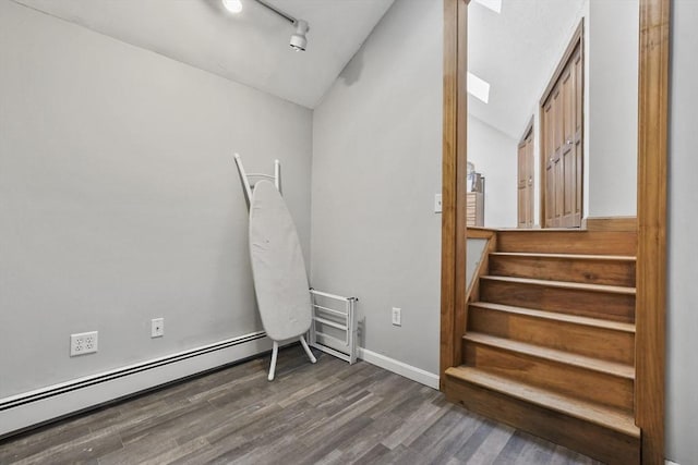 interior space with a baseboard heating unit, baseboards, lofted ceiling, rail lighting, and wood finished floors