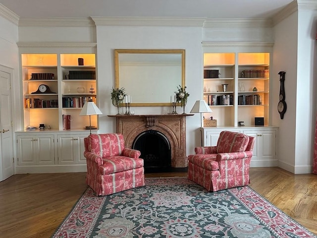 living area featuring wood finished floors, crown molding, a fireplace, and built in features