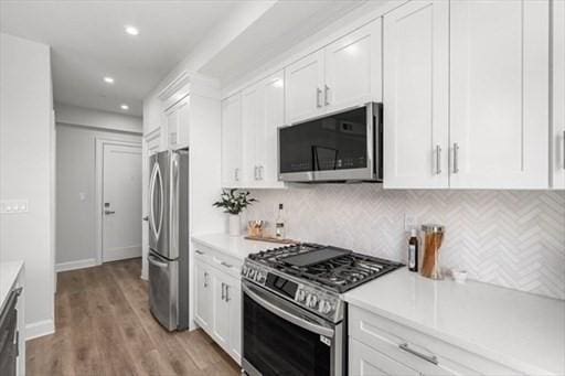 260 Elm St Unit 204, Everett, MA 02149 - kitchen with appliances with stainless steel finishes, white cabinets, light countertops, decorative backsplash, and light wood finished floors