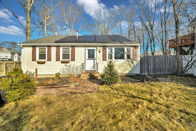 view of front of house with roof mounted solar panels, a front yard, and fence