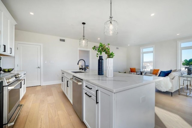 62 Foundry St Unit 215, Wakefield, MA 01880 - kitchen with appliances with stainless steel finishes, light wood-style flooring, white cabinetry, a kitchen island with sink, and hanging light fixtures