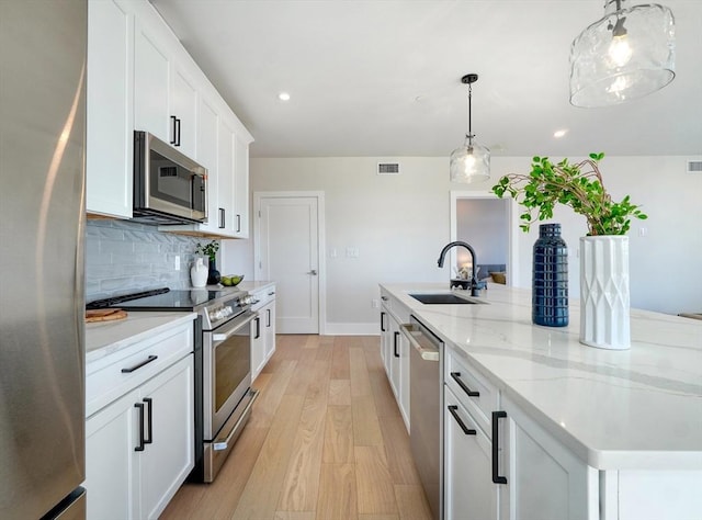 62 Foundry St Unit 215, Wakefield, MA 01880 - kitchen with appliances with stainless steel finishes, light wood-style floors, a large island with sink, decorative backsplash, and white cabinetry