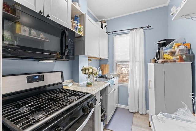 kitchen featuring white cabinets, gas stove, light wood-type flooring, and ornamental molding