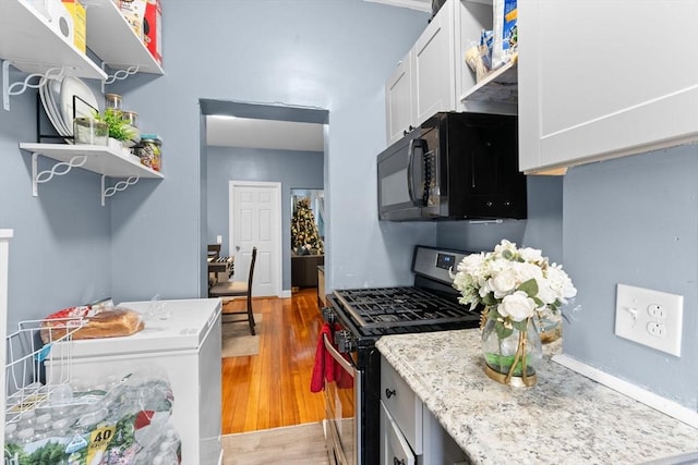 kitchen with gas range, white cabinetry, light stone counters, fridge, and light wood-type flooring