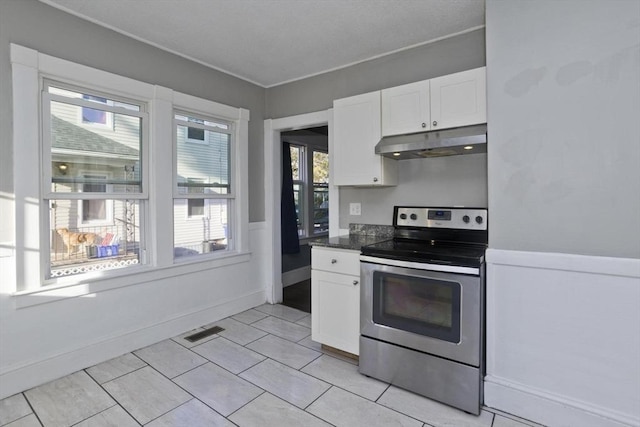 kitchen featuring under cabinet range hood, stainless steel electric range oven, white cabinets, dark countertops, and wainscoting