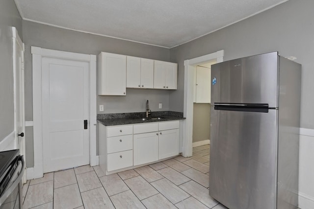 kitchen with stainless steel fridge, white cabinetry, a textured ceiling, stove, and sink