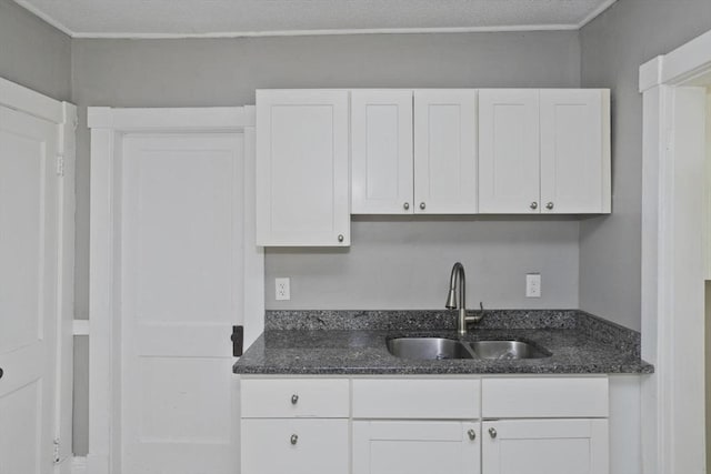 kitchen with a sink, white cabinets, and dark stone counters