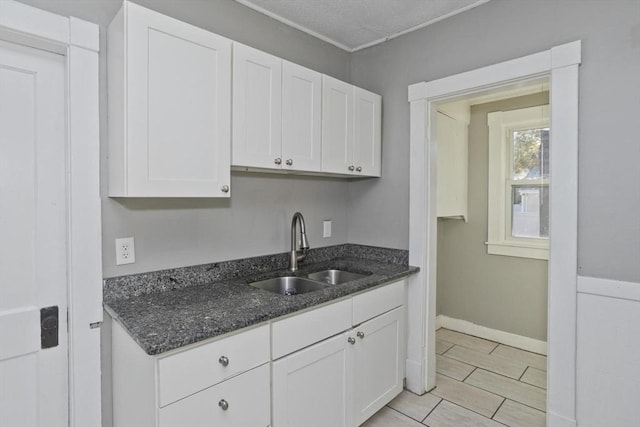 kitchen featuring a sink, white cabinets, dark stone counters, and baseboards
