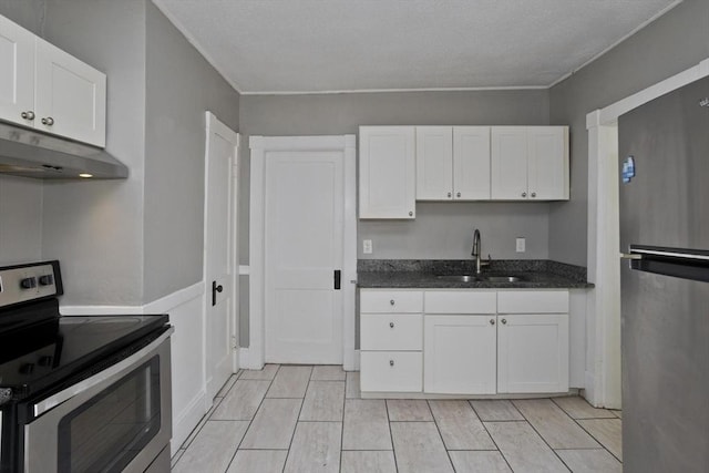 kitchen featuring appliances with stainless steel finishes, under cabinet range hood, a sink, white cabinets, and dark stone counters
