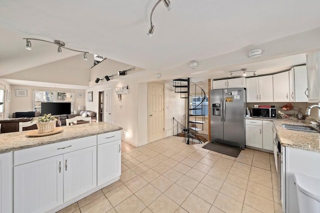 kitchen with a sink, white cabinetry, vaulted ceiling, open floor plan, and stainless steel fridge