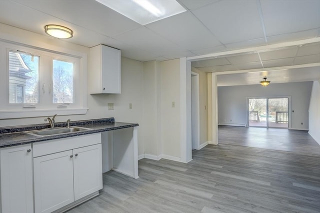 kitchen with a paneled ceiling, sink, white cabinets, and light wood-type flooring