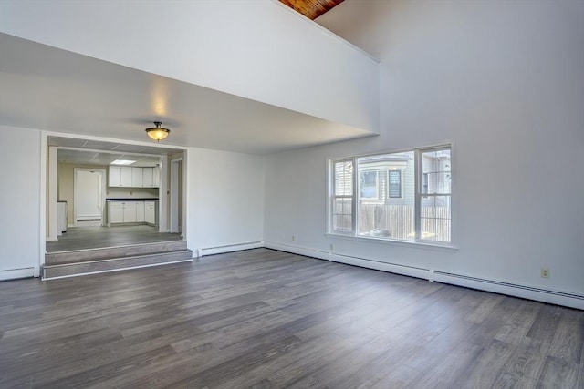 unfurnished living room with baseboard heating, dark wood-type flooring, and a high ceiling