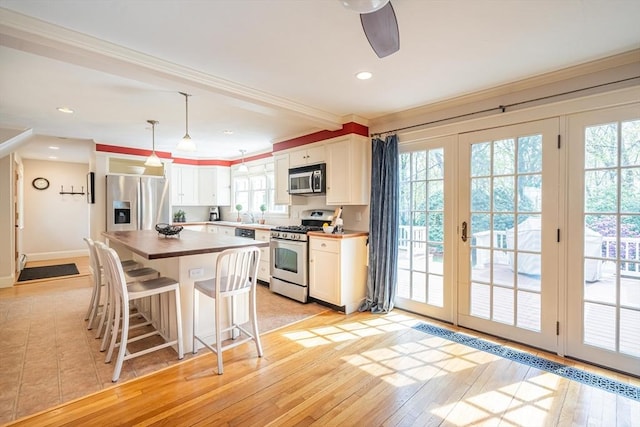 kitchen with crown molding, white cabinets, stainless steel appliances, light wood-type flooring, and pendant lighting