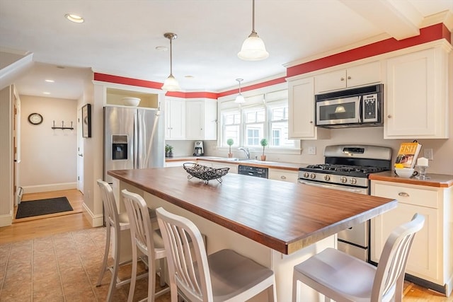 kitchen featuring stainless steel appliances, white cabinetry, butcher block counters, and a center island
