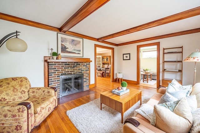 living room featuring a brick fireplace, baseboards, beamed ceiling, ornamental molding, and hardwood / wood-style flooring