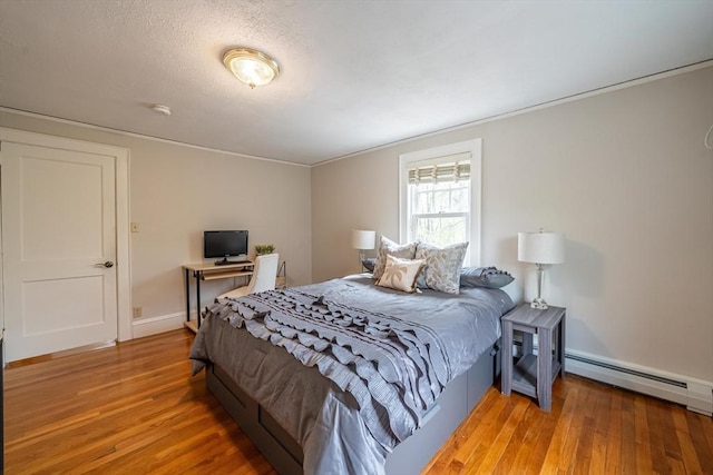 bedroom featuring baseboards, a baseboard heating unit, ornamental molding, and light wood-style floors