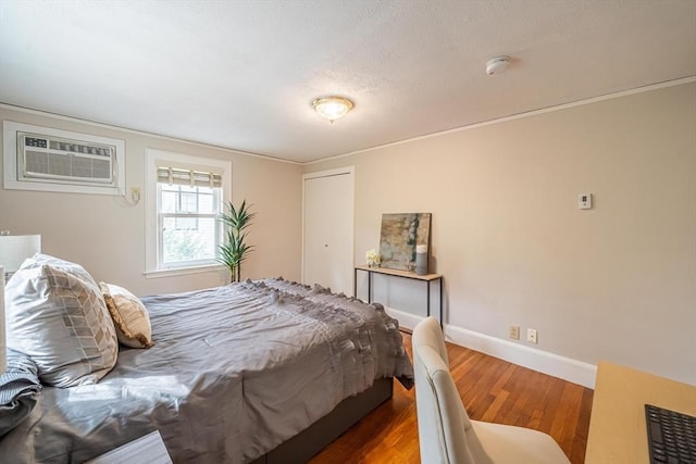 bedroom featuring a closet, baseboards, wood finished floors, and a wall mounted air conditioner