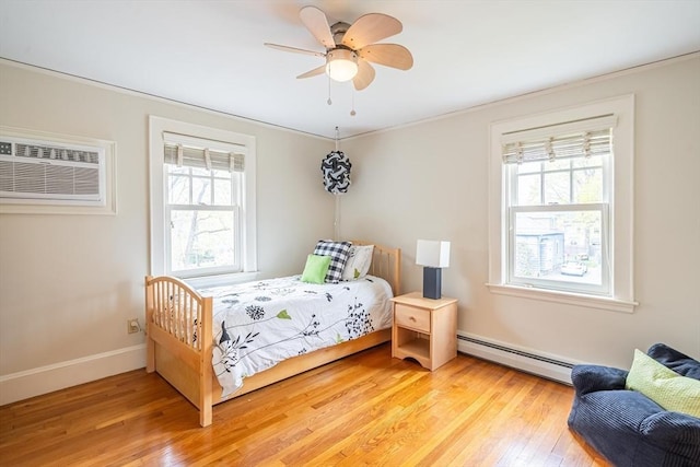 bedroom with a baseboard radiator, multiple windows, light wood finished floors, and a wall mounted air conditioner