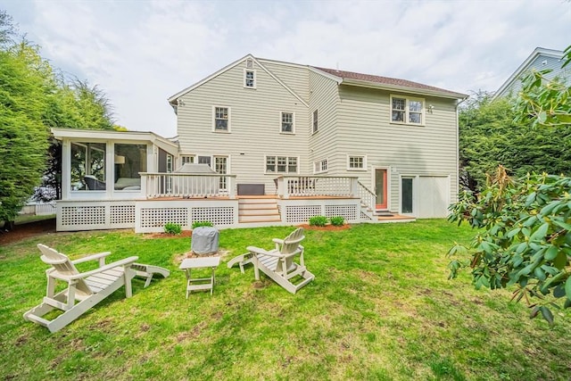 back of house featuring a lawn, a wooden deck, a sunroom, and a fire pit