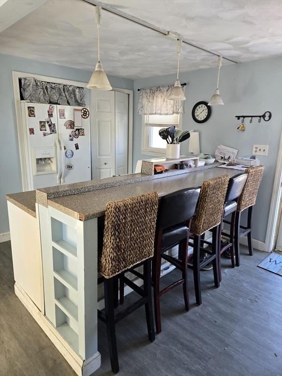 kitchen with hanging light fixtures, dark wood-type flooring, a breakfast bar area, and white fridge with ice dispenser