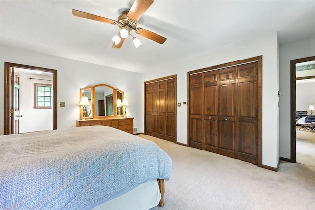 bedroom with two closets, light carpet, ceiling fan, and baseboards