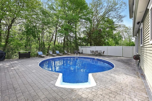view of swimming pool with a patio area, outdoor dining space, a fenced backyard, and view of wooded area