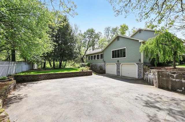 view of home's exterior featuring asphalt driveway, stone siding, a garage, and fence