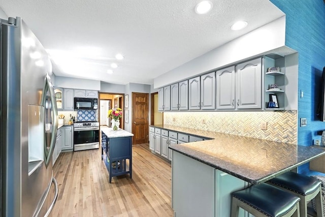 kitchen with appliances with stainless steel finishes, open shelves, a peninsula, gray cabinets, and a textured ceiling