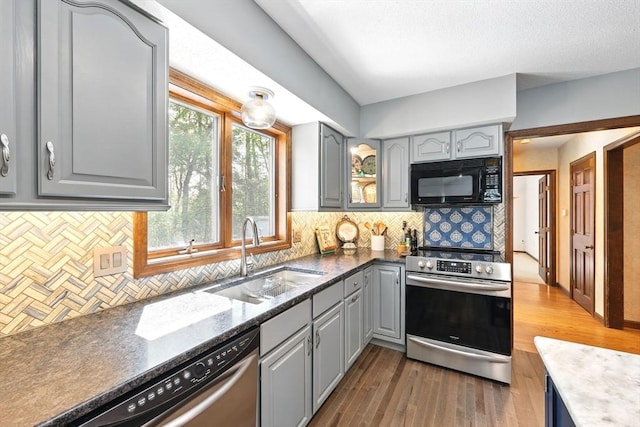 kitchen featuring appliances with stainless steel finishes, gray cabinets, a sink, wood finished floors, and backsplash