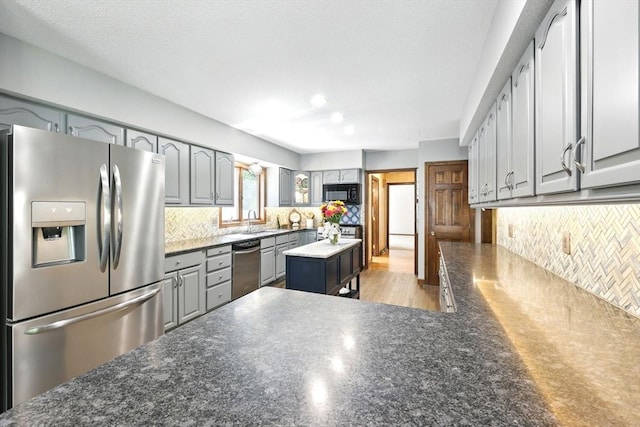 kitchen featuring stainless steel appliances, gray cabinetry, a sink, backsplash, and dark countertops
