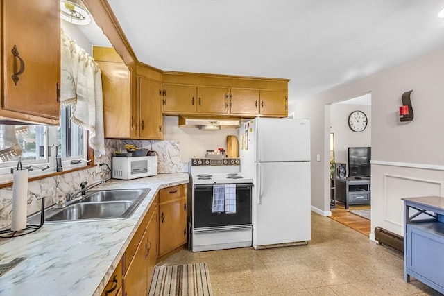 kitchen featuring white appliances, under cabinet range hood, light countertops, tasteful backsplash, and brown cabinets