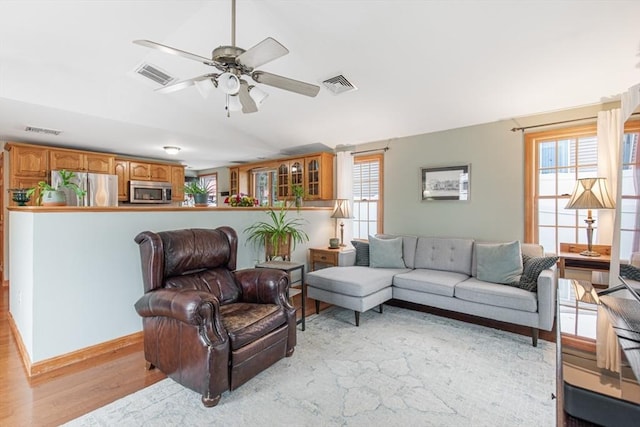 living area with light wood finished floors, healthy amount of natural light, a ceiling fan, vaulted ceiling, and baseboards