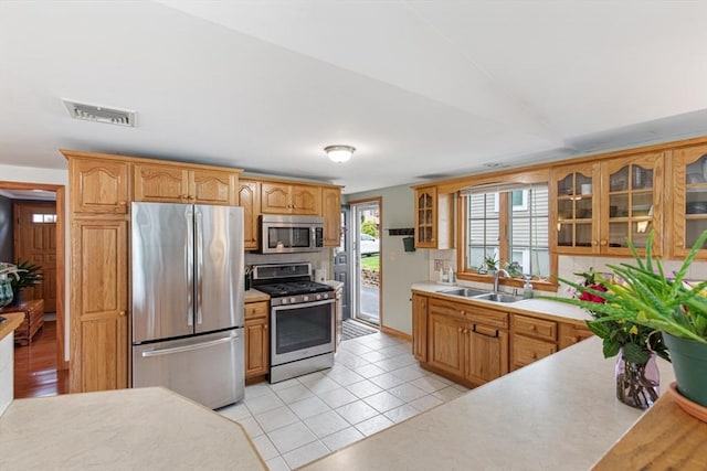kitchen with appliances with stainless steel finishes, a sink, glass insert cabinets, light tile patterned floors, and light countertops