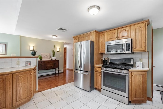 kitchen with stainless steel appliances, baseboard heating, light countertops, and decorative backsplash