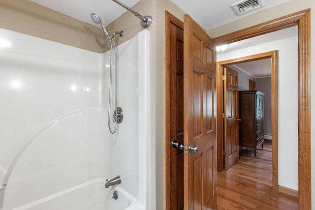 bathroom featuring wood finished floors, washtub / shower combination, a baseboard heating unit, crown molding, and baseboards