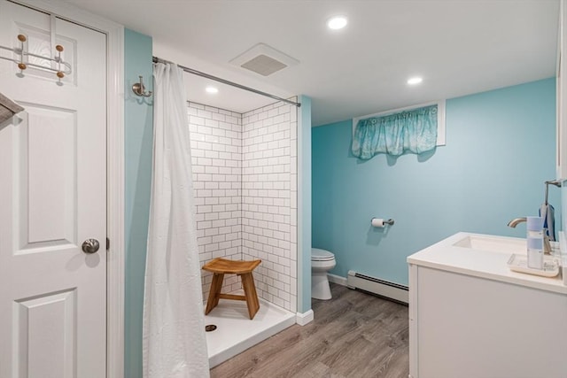 full bathroom featuring a baseboard radiator, a sink, wood finished floors, toilet, and a tile shower