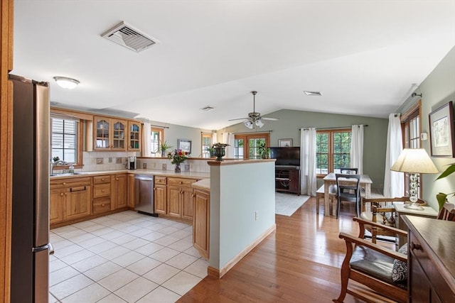 kitchen featuring stainless steel appliances, a peninsula, vaulted ceiling, decorative backsplash, and glass insert cabinets