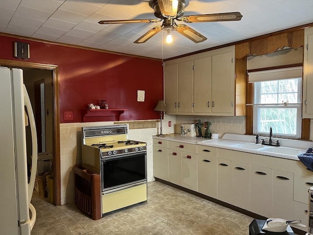 kitchen featuring refrigerator, sink, tile walls, white cabinets, and white range with gas stovetop